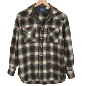 May include: A long-sleeved, button-down shirt in a plaid pattern of brown, cream, and teal. The shirt has two chest pockets with decorative snaps and a quilted collar. The Pendleton label is visible at the back of the collar.