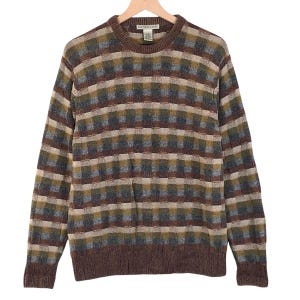 May include: A brown, green, and blue checked sweater with a crew neck, hanging on a wooden hanger. The sweater has long sleeves and a ribbed hem and cuffs. The brand name "GEORGE KASTEN" is visible on the label.