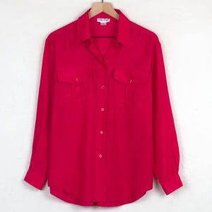 May include: A bright red long-sleeved button-down shirt with two chest pockets. The shirt is hanging on a wooden hanger. The label reads "Anne & Frank".