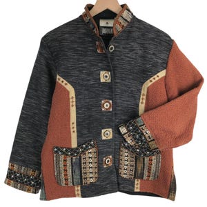 May include: A long-sleeved jacket featuring a dark gray heathered body with rust-colored textured side panels. It has a mandarin collar, a front button closure with square buttons, and two front pockets with patterned fabric and sequin accents.