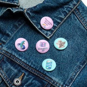 May include: Five circular pin badges with different designs. One badge reads "Dead inside but still horny". Other badges feature a dolphin in a ring, a Windows XP logo, an angel, and a can of "Tears".