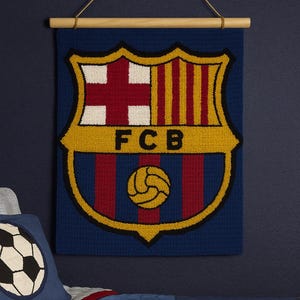 May include: A blue wall hanging featuring the FC Barcelona crest. The crest includes a red cross, vertical stripes, and a soccer ball. The hanging is suspended from a wooden rod with a gold cord.