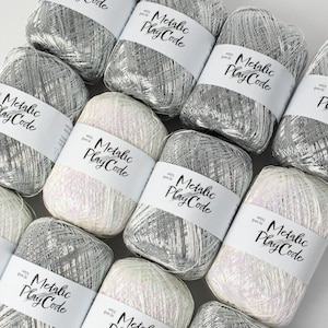 May include: Close-up of several spools of metallic yarn in shades of silver and white. Each spool has a white label with the text "Metallic Play Code". The yarn appears soft and is ideal for crafting projects.