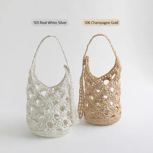 May include: Two crochet handbags, one in Real White Silver and the other in Champagne Gold. Each bag has a rounded bottom, openwork design, and a single handle. The bags are displayed against a white background.