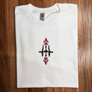 A white t-shirt with a red and black embroidered design on the front.