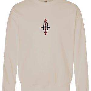 A beige sweatshirt with a small red and black embroidered design on the front.