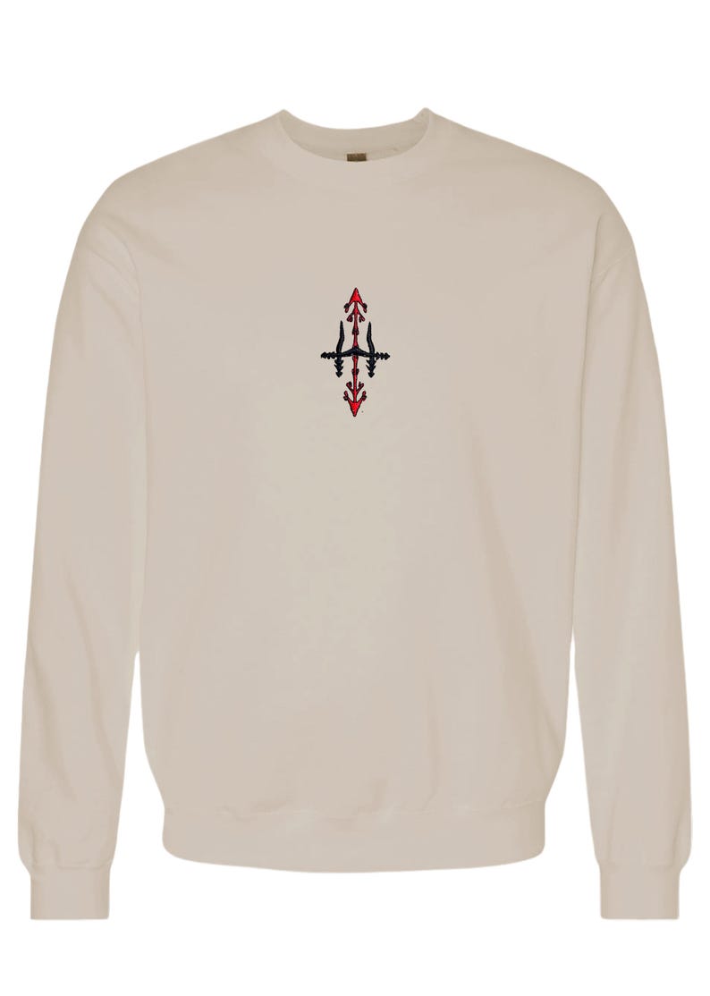 A beige sweatshirt with a small red and black embroidered design on the front.