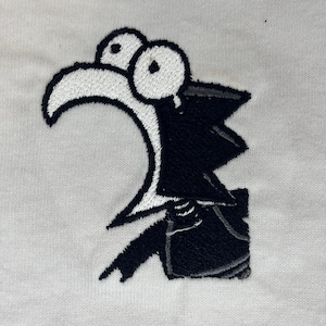May include: Embroidered patch showing a cartoon character with a large white beak, big eyes, and a black outfit. The design is stitched on a white fabric background. The character is pointing with its right hand.