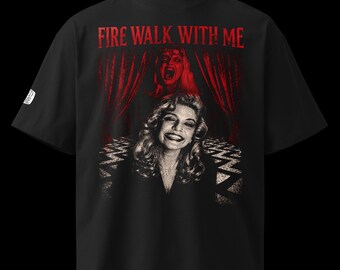 May include: A black t-shirt featuring a graphic print with the text "FIRE WALK WITH ME" in red. The design displays a smiling person in the foreground, a screaming figure above, red curtains, and a black and white chevron floor pattern.