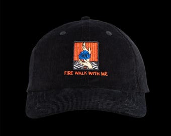 May include: A black corduroy baseball cap featuring an embroidered rectangular patch on the front. The patch displays a hand holding a blue rose against an orange background, with the text FIRE WALK WITH ME embroidered in orange below it.