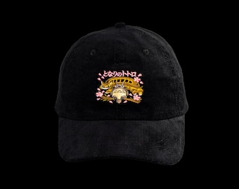 May include: A black corduroy baseball cap featuring an embroidered graphic of a cat-shaped bus and a small creature on a branch, surrounded by pink cherry blossom petals. Above the graphic is the Japanese text となりのトトロ in pink.