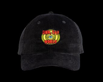 May include: A black corduroy baseball cap featuring an embroidered patch on the front. The patch displays a yellow and green circular design with a central blue eye and the red text SICK SAD WORLD written in a dripping, stylized font.