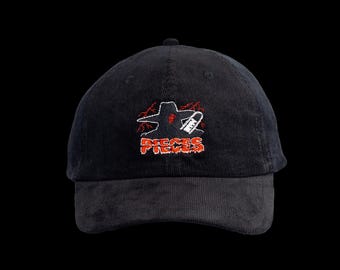 May include: A black corduroy baseball cap featuring an embroidered graphic on the front. The design depicts a dark silhouette with red lightning bolts and a white chainsaw, positioned above the red text PIECES in a distressed, jagged font style.