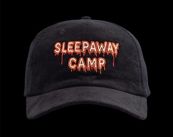 May include: Black corduroy baseball cap with the text "SLEEPAWAY CAMP" in orange and red dripping font. The cap has a curved brim and a button on top. The hat is set against a black background.