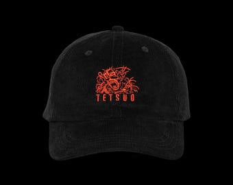 May include: A black corduroy baseball cap featuring an embroidered red graphic of a stylized, screaming face with intricate line work and the text TETSUO in red capital letters centered on the front panel above the curved brim.