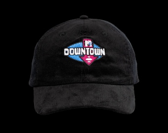 May include: A black corduroy baseball cap featuring an embroidered logo on the front. The logo consists of a blue diamond shape with a pink downward-pointing arrow and the white text DOWNTOWN, topped with a small MTV logo icon.