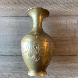 May include: A brass vase with an etched leaf design. The vase has a flared top and a rounded body. The brass has a warm, golden hue. The vase is approximately 20 cm tall.