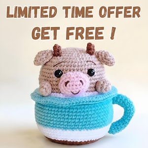 May include: A crocheted cow toy in a blue and white cup. The cow is light brown with a pink nose and black eyes. The cup has a blue handle and the text "LIMITED TIME OFFER GET FREE!"