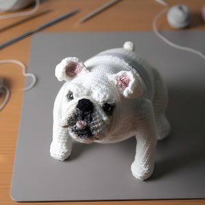 May include: A white crochet bulldog ornament with pink ear interiors and a black nose. The dog is depicted standing, highlighting the intricate crochet work. This bulldog is a delightful decorative piece.