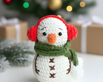 May include: A handmade crochet snowman with a red earmuffs, green scarf, and an orange carrot nose. The snowman has brown stitched details and a white pompom. Christmas decor.