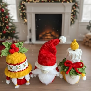 May include: Three handmade crochet Christmas gnomes. One gnome wears a yellow hat with holly, another a red Santa hat, and the third a candle-shaped hat. Each gnome has a white beard and is decorated with red and green accents. Festive holiday decor.