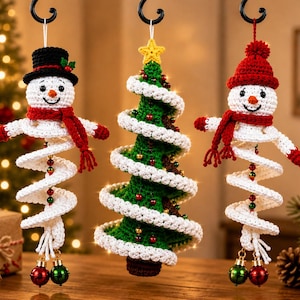 Puede incluir: Tres adornos colgantes de ganchillo que representan dos muñecos de nieve y un árbol de Navidad. Los muñecos llevan sombreros negros o rojos y bufandas rojas, con cuerpos en espiral blanca que terminan en cascabeles.