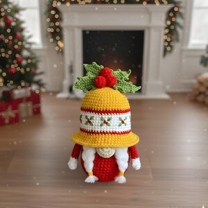 May include: A handmade crochet gnome doll with a yellow hat, red body, and white beard. The hat is decorated with a red and white band and green holly leaves with red berries. The gnome is a festive holiday decoration.