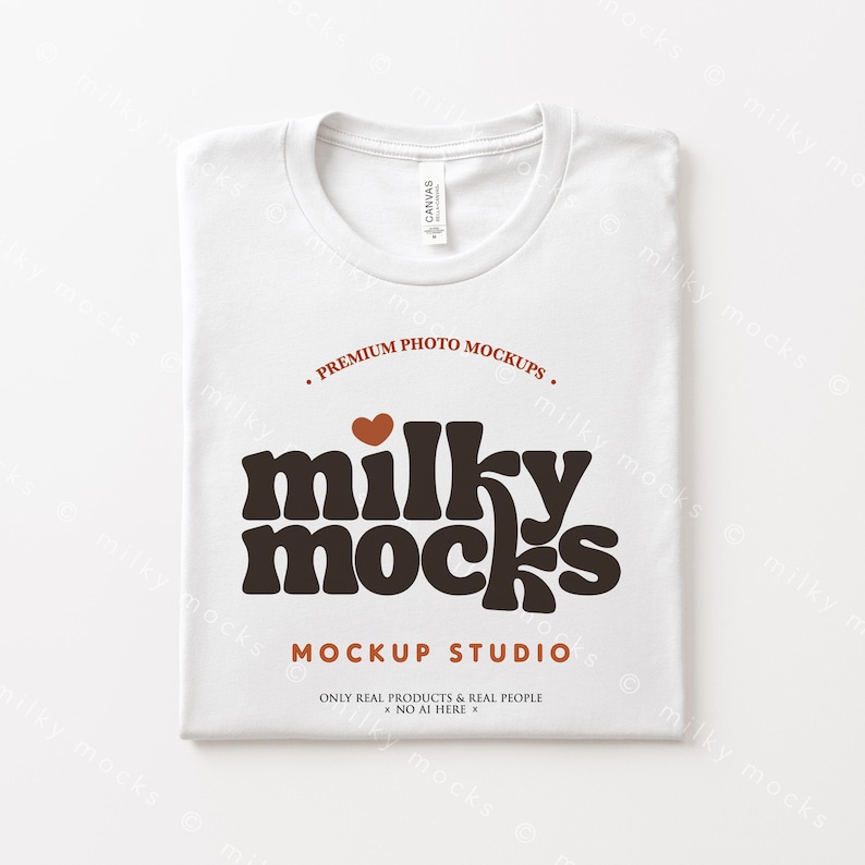Puede incluir: Una camiseta blanca doblada con cuello redondo. La camiseta presenta el texto "milky mocks" en una fuente marr&oacute;n retro, con un peque&ntilde;o coraz&oacute;n encima de la palabra. El texto adicional incluye "PREMIUM PHOTO MOCKUPS" y "MOCKUP STUDIO."