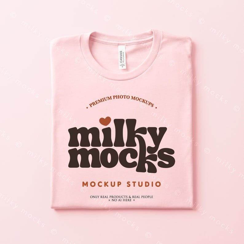 Puede incluir: Una camiseta rosa claro doblada con las palabras "milky mocks" en marr&oacute;n, un coraz&oacute;n marr&oacute;n y el texto "MOCKUP STUDIO". La camiseta tiene una etiqueta "CANVAS". Tambi&eacute;n es visible el texto "ONLY REAL PRODUCTS & REAL PEOPLE x NO AI HERE".
