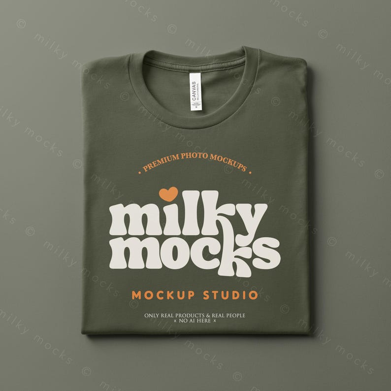 Puede incluir: Camiseta verde oliva doblada, con cuello redondo. La camiseta presenta el texto "milky mocks" en una fuente retro, con un coraz&oacute;n naranja. Tambi&eacute;n son visibles las palabras "MOCKUP STUDIO" y "ONLY REAL PRODUCTS & REAL PEOPLE".