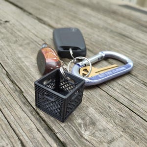 May include: A collection of keys and keychains on a wooden surface. The keychains include a miniature black crate, a wooden bird, and a car key fob. A silver and blue carabiner clip holds a key with the text "NOT FOR CLIMBING".