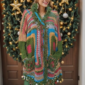 May include: A woman wearing a colourful crocheted cardigan with fringe details. The cardigan is made with a variety of colours, including green, blue, pink, and yellow. The woman is also wearing a green hat with a red pom-pom.