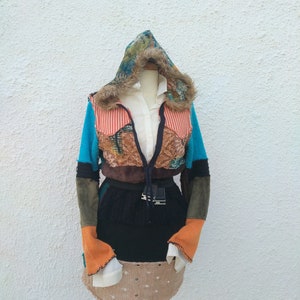 Peut inclure: Veste patchwork colorée avec capuche et garniture en fausse fourrure, présentée sur un mannequin. La veste présente un mélange de textures et de couleurs, notamment le bleu sarcelle, l'orange et le marron. Une chemise blanche à col et une jupe noire sont également visibles.