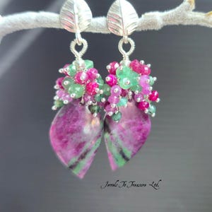 May include: A pair of drop earrings featuring silver leaf-shaped tops, clusters of small faceted green and pink beads, and large teardrop-shaped pink and green stone pendants. The text Jewels To Treasure Ltd. is visible at the bottom right.
