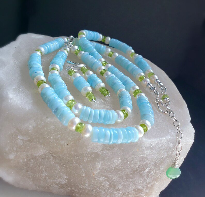 K&ouml;nnte beinhalten: Ein Set aus blauem und wei&szlig;em Edelsteinschmuck mit gr&uuml;nen Akzenten. Das Set beinhaltet eine Halskette, ein Armband und Ohrringe.
