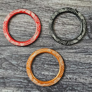 May include: Three decorative rings with a white patterned design. The rings are red, black, and orange.