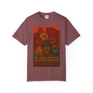 May include: A maroon t-shirt featuring a graphic of Dr. Teeth and The Electric Mayhem. The design includes the band members and text that reads "DR. TEETH AND THE ELECTRIC MAYHEM RED ROCKS AMPHITHEATRE MORRISON, CO MARCH 18, 1975."