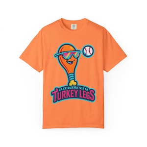 May include: Orange t-shirt featuring a cartoon turkey leg wearing sunglasses and a baseball. The text "Lake Buena Vista Turkey Legs" is below the graphic. The shirt is a crew neck style.