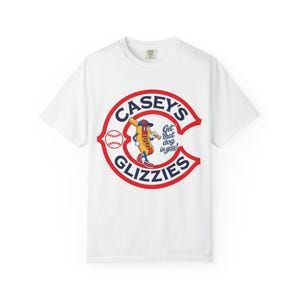 May include: White t-shirt featuring a baseball-themed graphic. The design includes a red and blue circular logo with the text "Casey's Glizzies" and a cartoon hot dog character holding a baseball bat. The shirt has a crew neck.