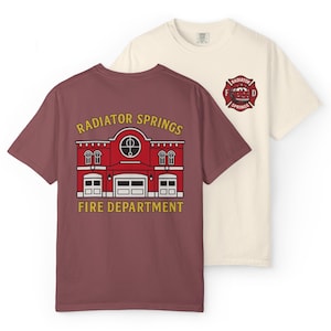 May include: Two t-shirts, one maroon and one cream, featuring graphics. The maroon shirt displays a red fire station graphic with the text "RADIATOR SPRINGS FIRE DEPARTMENT." The cream shirt has a fire department logo with the text "RADIATOR SPRINGS."