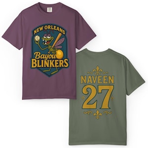 May include: Two t-shirts: one purple, one olive green. The purple shirt features a cartoon insect holding a baseball bat, with text reading "New Orleans Bayou Blinkers." The olive green shirt displays the name "Naveen" and the number "27."