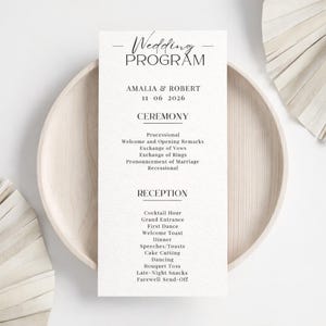 K&ouml;nnte beinhalten: Ein Hochzeitsprogramm mit dem Titel "Wedding Program" oben. Das Programm enth&auml;lt die Namen "AMALIA & ROBERT" und das Datum "11 06 2026". Das Programm listet die Zeremonie- und Empfangsereignisse auf, gedruckt auf strukturiertem wei&szlig;em Papier.