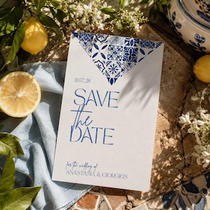 Puede incluir: Una tarjeta rectangular de save the date con un patrón de azulejos mediterráneos en azul y blanco en la parte superior. El texto dice 11.07.28, SAVE THE DATE, y for the wedding of ANASTASIA & GIORGIOS en fuente azul sobre fondo blanco.