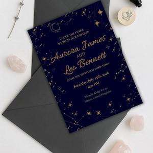 May include: Dark blue wedding invitation with gold star and constellation design. The invitation reads "Aurora James and Leo Bennett" and includes the date, time, and location of the ceremony. The invitation is placed on a dark grey envelope.