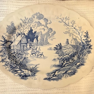 Può includere: Un piatto da portata ovale in ceramica con bordo smerlato, caratterizzato da una scena in blu e bianco che raffigura un paesaggio rurale con un cottage, alberi e cavalli. Il testo "Harnessing the Team" è stampato in basso a sinistra.