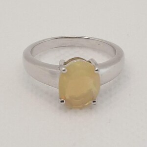 May include: A silver ring featuring a large, oval-cut, light yellow gemstone. The gemstone is held in place by four prongs. The ring band is a simple, polished silver.