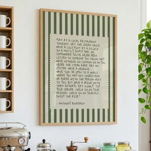 Striped Anthony Bourdain typography poster with handwritten text on a warm cream background featuring olive green, navy blue, and charcoal black colour variations. Vintage-inspired kitchen wall art with subtle stripe details and European cafe aesthetic displayed in wooden frames inside cozy interiors. Minimal quote print designed for coffee corners, dining rooms, bookstores, restaurants, and modern apartments with warm lighting and neutral decor styling.
