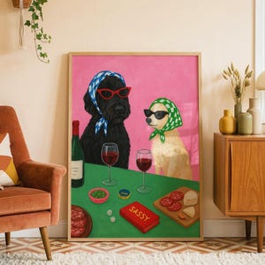 May include: A framed art print depicting two dogs enjoying wine and snacks. One dog is wearing a blue and white headscarf and red sunglasses, the other a green and white scarf and black sunglasses. A red box reads "Sassy".