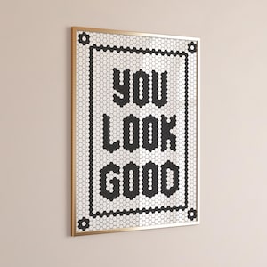 May include: Framed wall art with the words "YOU LOOK GOOD" in black block letters. The text is set against a white background of small hexagonal tiles, framed by a gold border.