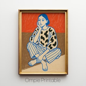 May include: A framed art print featuring a seated figure with blue hair and clothing. The figure is wearing a patterned top and striped pants. The background is divided into red and brown sections. The print is in a gold frame.